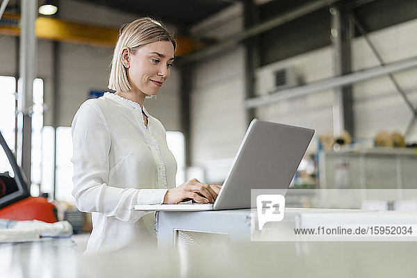 Smiling young woman using laptop in a factory