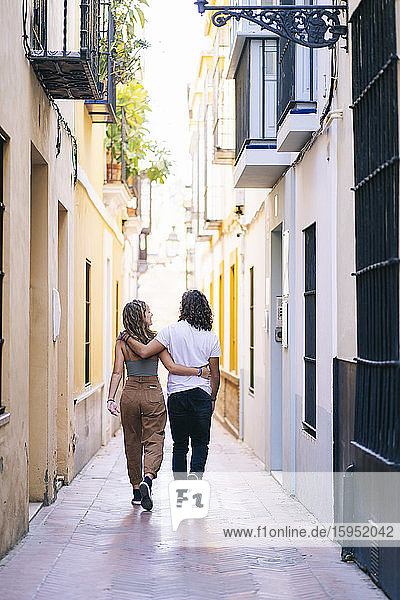 Rear view of young couple walking with arms around on narrow street at Santa Cruz  Seville  Spain