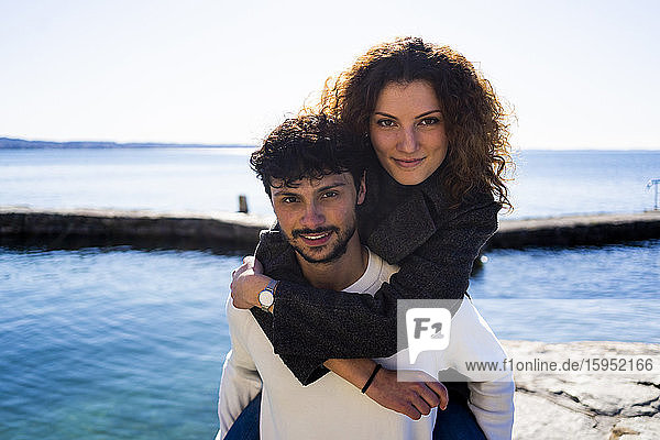 Portrait of young man carrying girlfriend piggyback at Lake Garda  Italy