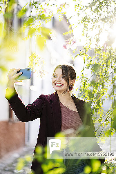 Lächelnde Frau  die sich in einer malerischen Gasse in der Stadt ein Selfie gönnt