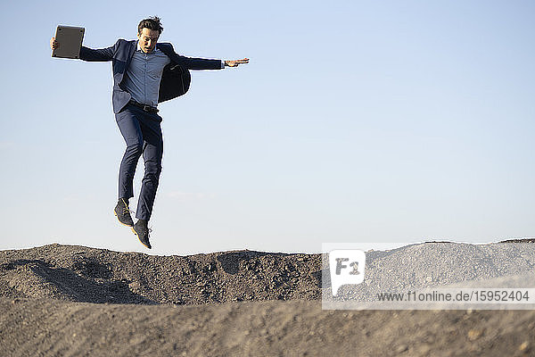 Mature businessman with laptop jumping on a disused mine tip