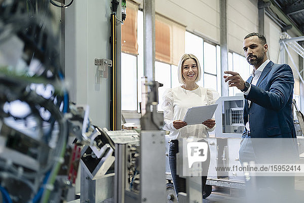 Geschäftsmann und junge Frau mit Papieren im Gespräch an einer Maschine in einer Fabrik