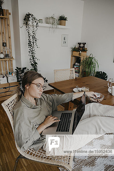 Frau benutzt Laptop  während sie im Home-Office mit erhobenen Füßen am Tisch sitzt
