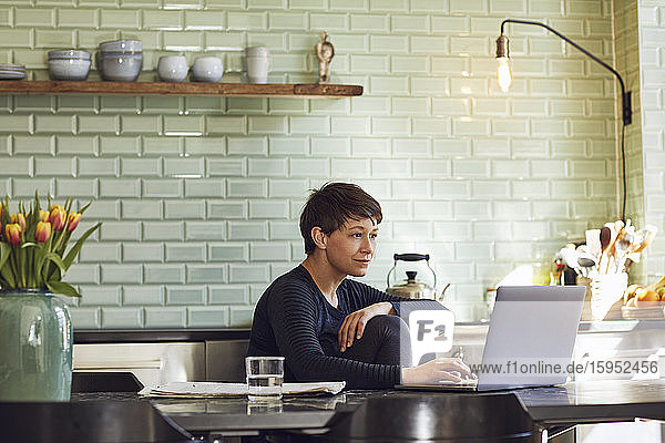Frau sitzt zu Hause mit Laptop am Küchentisch