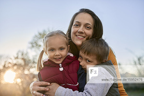 Porträt einer glücklichen Mutter  die zwei Kinder im Freien umarmt