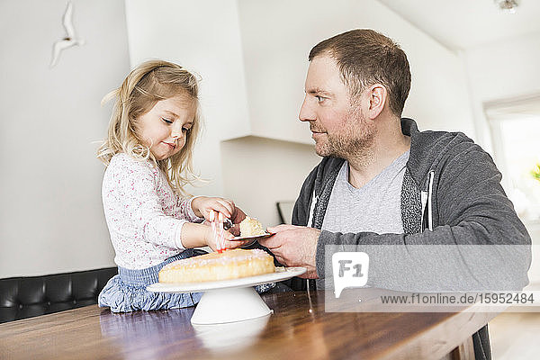 Vater und Tochter spielen mit einem Puppengeschirr und einem Stück Kuchen auf einem Teller