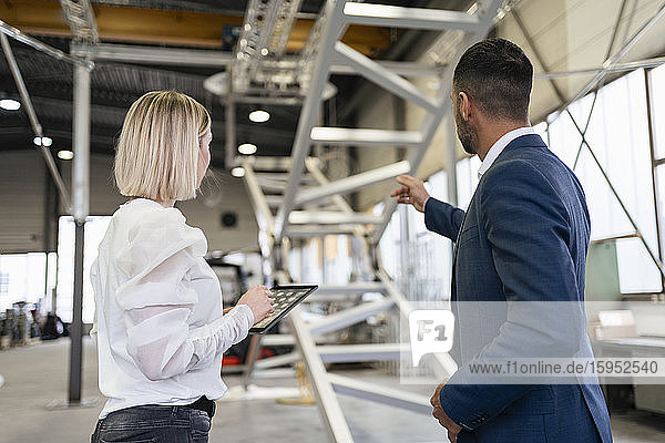 Businessman and young woman with tablet talking in a factory
