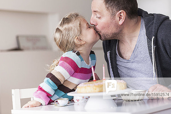 Vater und Tochter spielen mit dem Puppengeschirr  küssen sich gegenseitig
