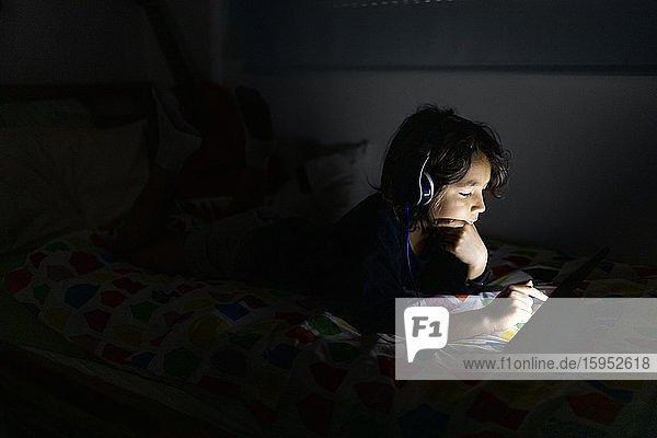 Junge liegt zu Hause im Bett und benutzt Kopfhörer und digitales Tablett
