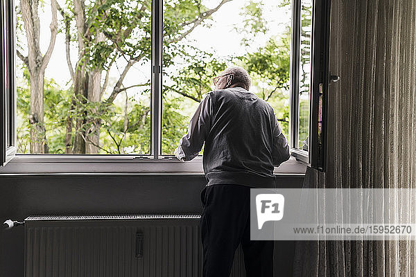 Rückenansicht eines älteren Mannes  der aus dem Fenster schaut