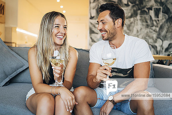 Porträt eines glücklichen Paares auf der Couch sitzend mit Weißweingläsern