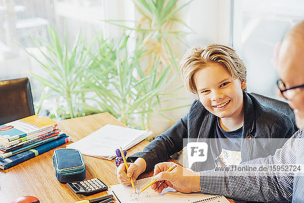 Porträt eines lächelnden Jungen mit einem Vater  der am Schreibtisch Hausaufgaben macht
