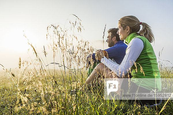 Couple sitting on a meadow in the mountains at dawn  Achenkirch  Austria