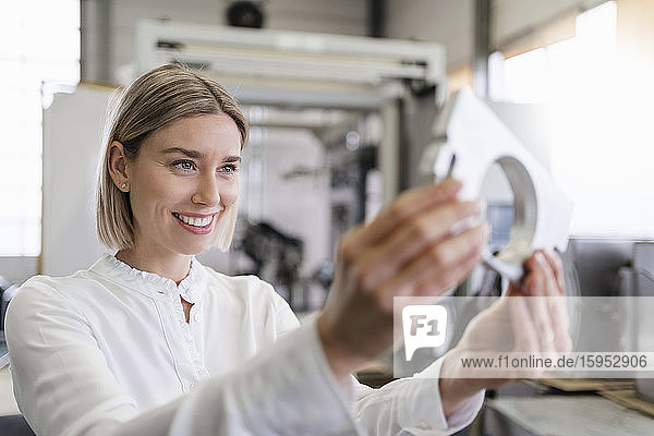 Smiling young woman holding workpiece in a factory