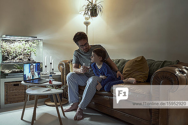 Arzt per Videoanruf mit krankem Mädchen und ihrem Vater über Laptop zu Hause