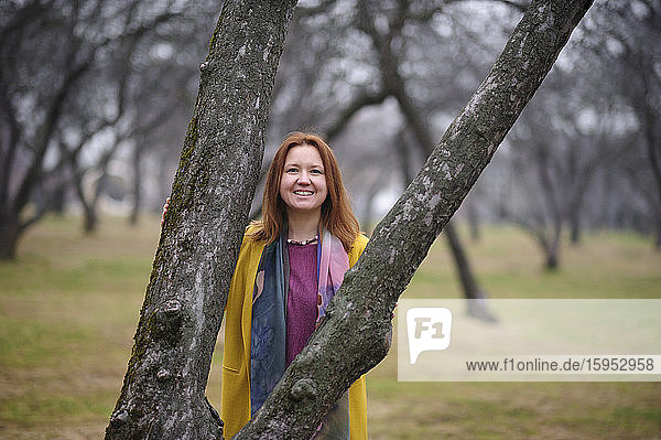 Porträt einer lächelnden Frau  die im Park an einem kahlen Baum steht