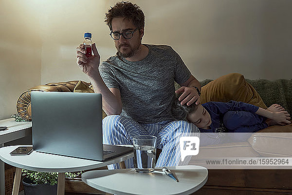 Man discussing telemedicine with doctor over video call through laptop while sitting by sick daughter in living room at home