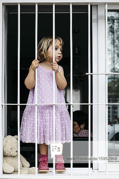 Girl standing at open window looking through window grate