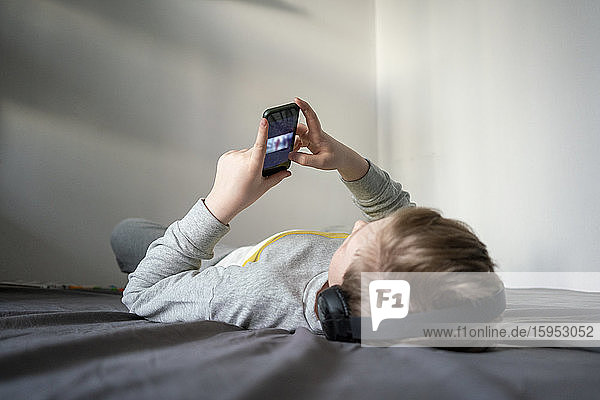 Boy with headphones lying on bed using cell phone