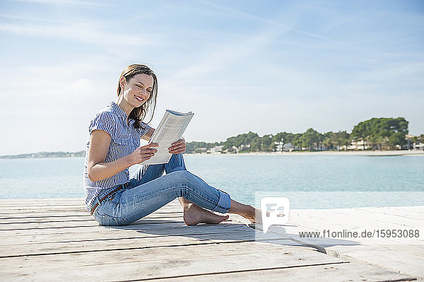 Frau sitzt am Steg und liest Zeitschrift  Mallorca  Spanien