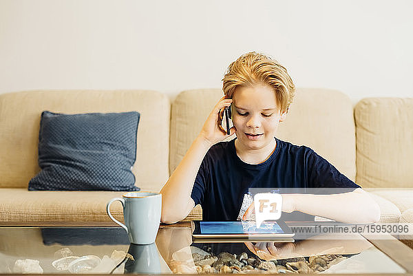 Junge benutzt zu Hause im Wohnzimmer Smartphone und Tablet