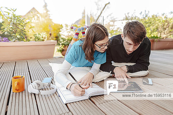 Teenager-Paar liegt auf der Terrasse und lernt gemeinsam mit dem digitalen Tablet