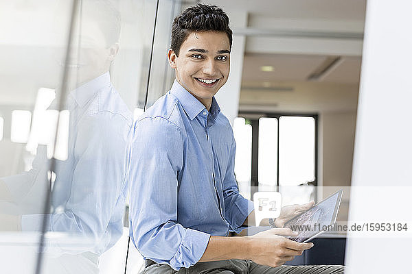 Portrait of smiling young businessman with tablet at the window in office