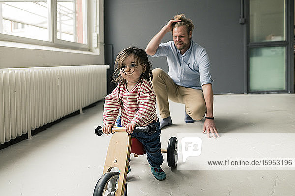 Lächelnder Vater beobachtet Tochter mit Balance-Fahrrad