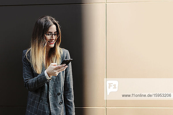 Lächelnde junge Geschäftsfrau schaut auf Handy