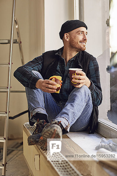 Mann renoviert Ladenstandort  sitzt auf der Fensterbank  trinkt Kaffee