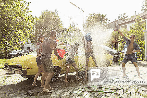 Eine Gruppe von Freunden wäscht im Sommer einen gelben Oldtimer und amüsiert sich
