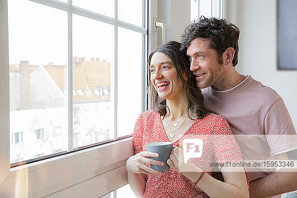Happy couple at home looking out of window