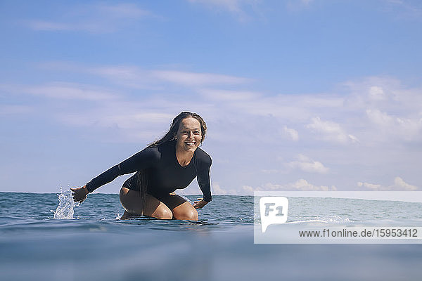 Porträt einer glücklichen Frau  die auf einem Surfbrett im Meer kniet  Bali  Indonesien