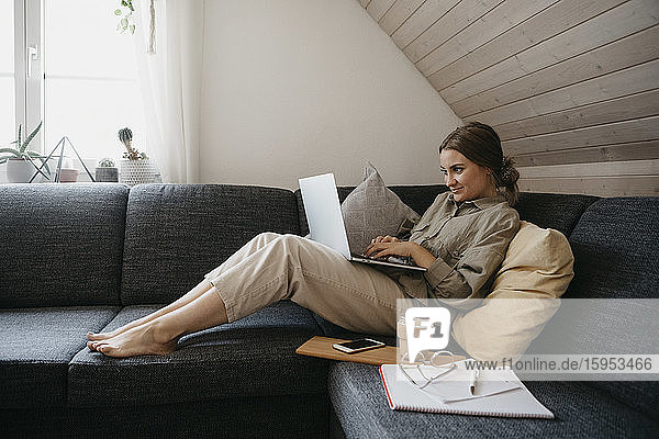 Frau benutzt Laptop  während sie zu Hause auf dem Sofa sitzt