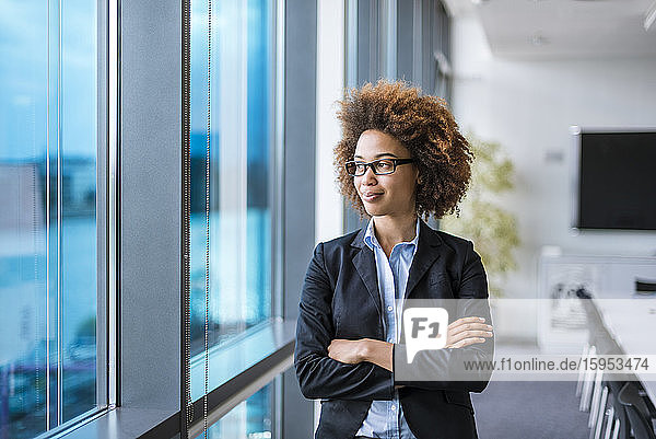 Porträt einer selbstbewussten jungen Geschäftsfrau im Konferenzraum  die aus dem Fenster schaut