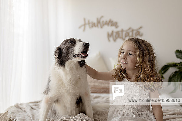 Porträt eines kleinen Mädchens  das mit seinem Hund auf dem Bett sitzt