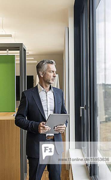 Mature businessman with tablet in office looking out of window
