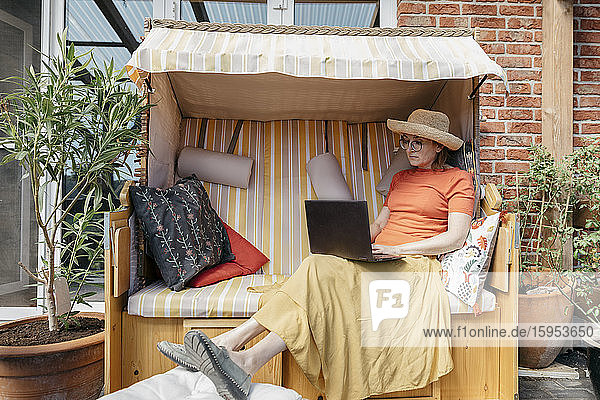 Reife Frau sitzt auf der Terrasse und arbeitet am Laptop