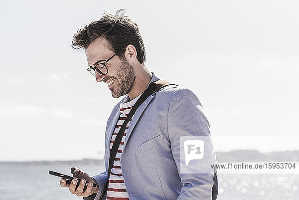 Smiling young man using smartphone on the waterfront