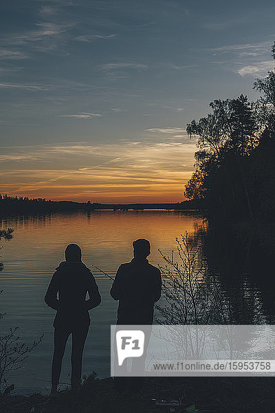 Couple standing at lake  fishing in lake at sunset