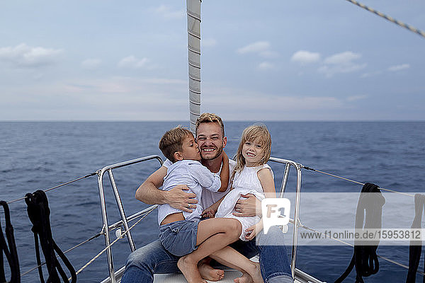 Vater mit seinen Kindern sitzt während der Segelfahrt auf dem Bootsdeck