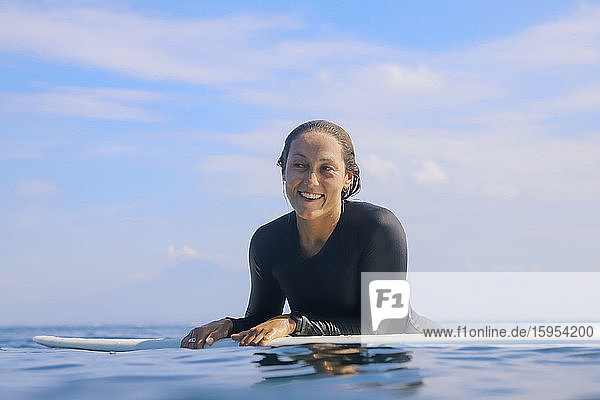 Porträt einer glücklichen Frau  die auf einem Surfbrett im Meer liegt  Bali  Indonesien