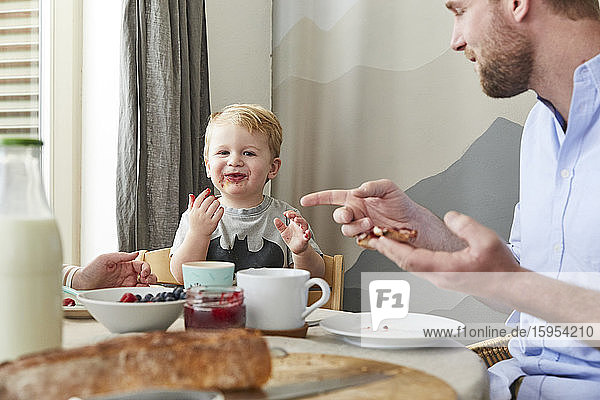 Porträt eines glücklichen kleinen Jungen am Frühstückstisch mit seinen Eltern