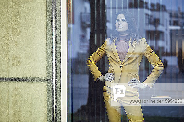 Selbstbewusste Geschäftsfrau im gelben Anzug hinter der Fensterscheibe stehend