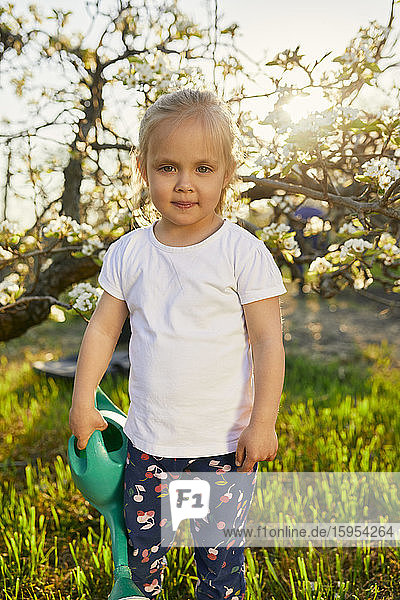 Porträt eines süßen blonden Mädchens  das am Wochenende im Garten steht und eine Gießkanne hält
