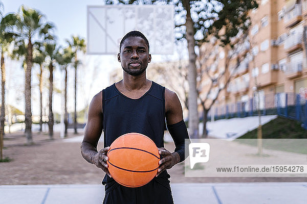 Junger Mann hält Basketball auf Basketballfeld
