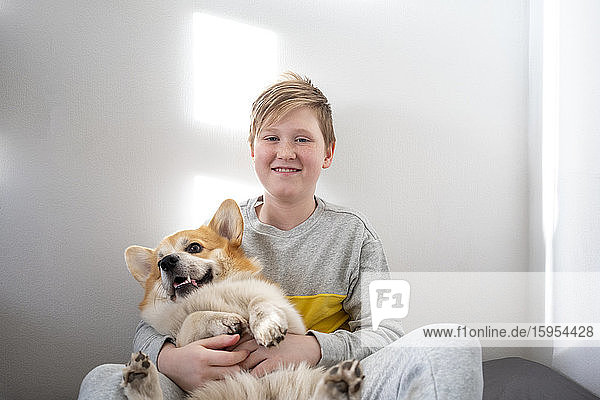 Portrait of boy sitting on bed at home cuddling his dog