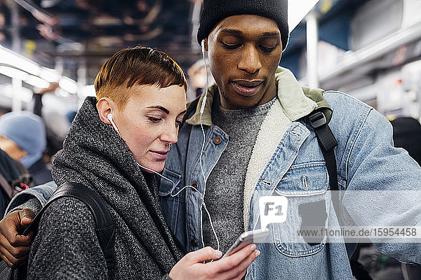 Young couple with earbuds using smartphone on a subway