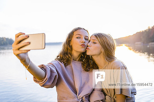 Friends puckering lips while taking selfie on smart phone against lake