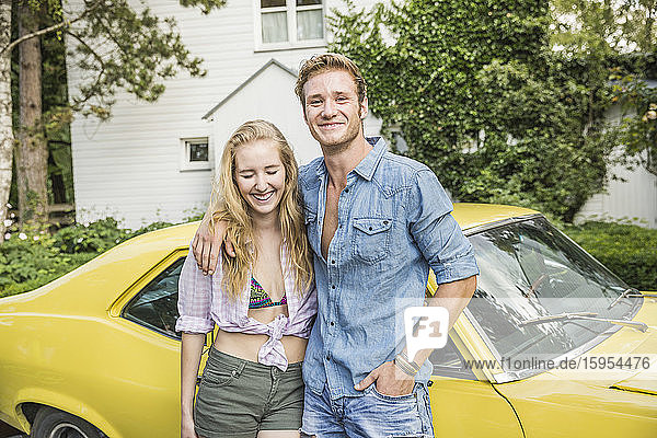 Porträt eines jungen Paares  das im Sommer vor einem gelben Oldtimer steht